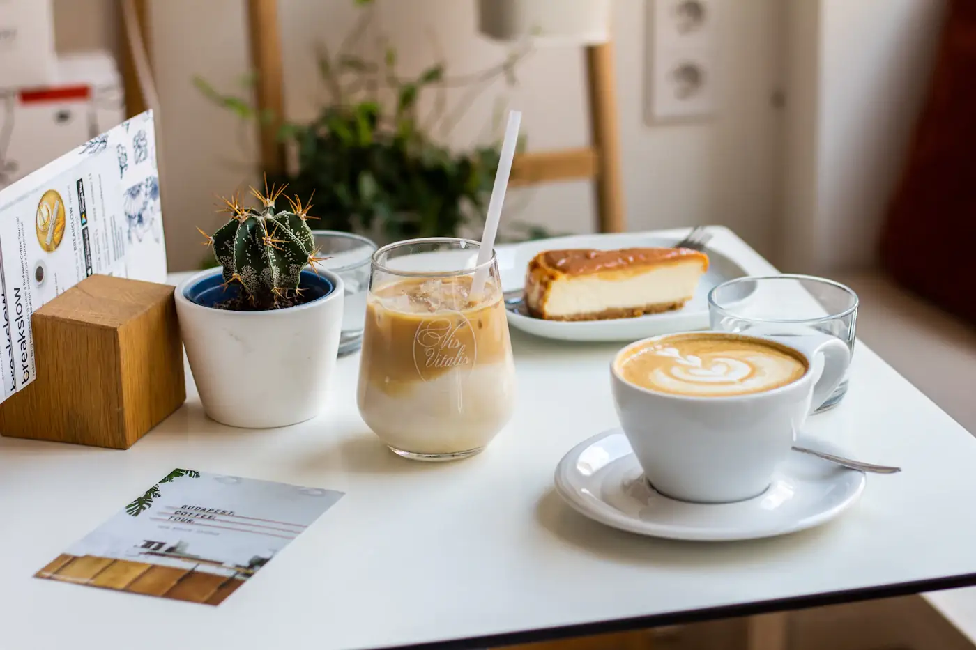 Cappuccino, ľadová káva a kúsok cheesecaku na bielom kaviarenskom stolíku